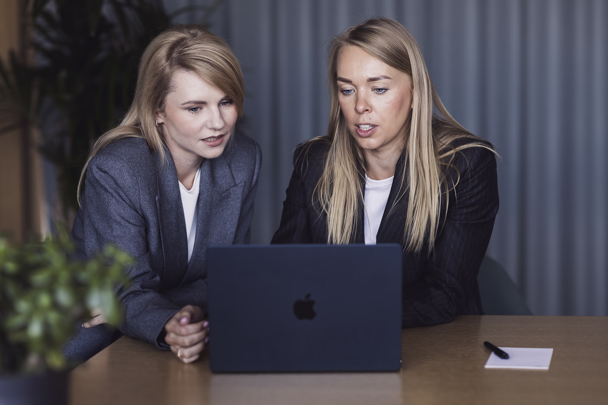 Two colleagues sit side by side reviewing something on a laptop during a workplace discussion.