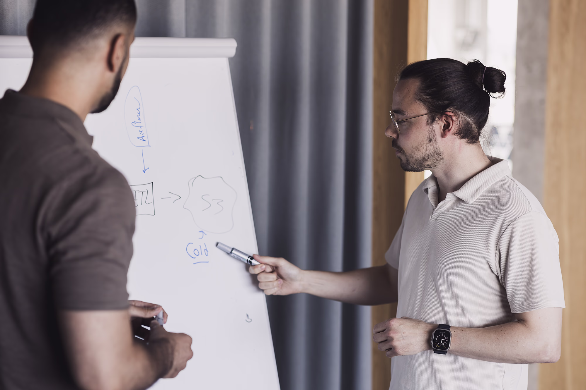 Two colleagues discuss a technical diagram on a flip chart during a planning session.
