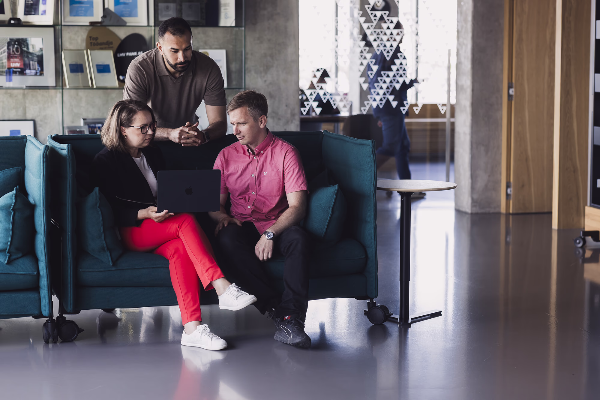Three colleagues gather around a laptop on a lounge sofa for an informal team discussion.